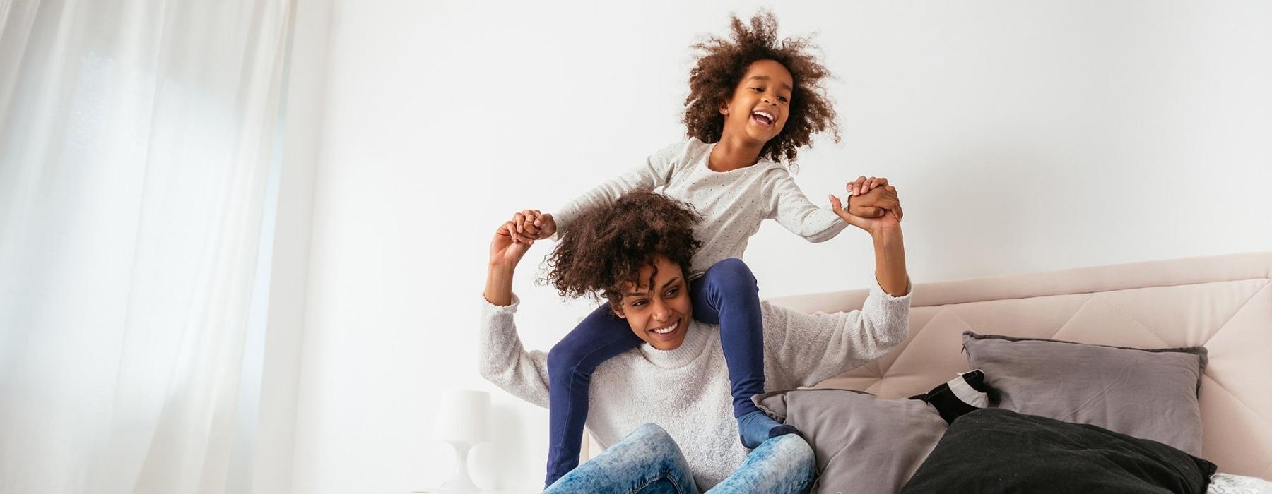 mother and daughter happily play on a large bed